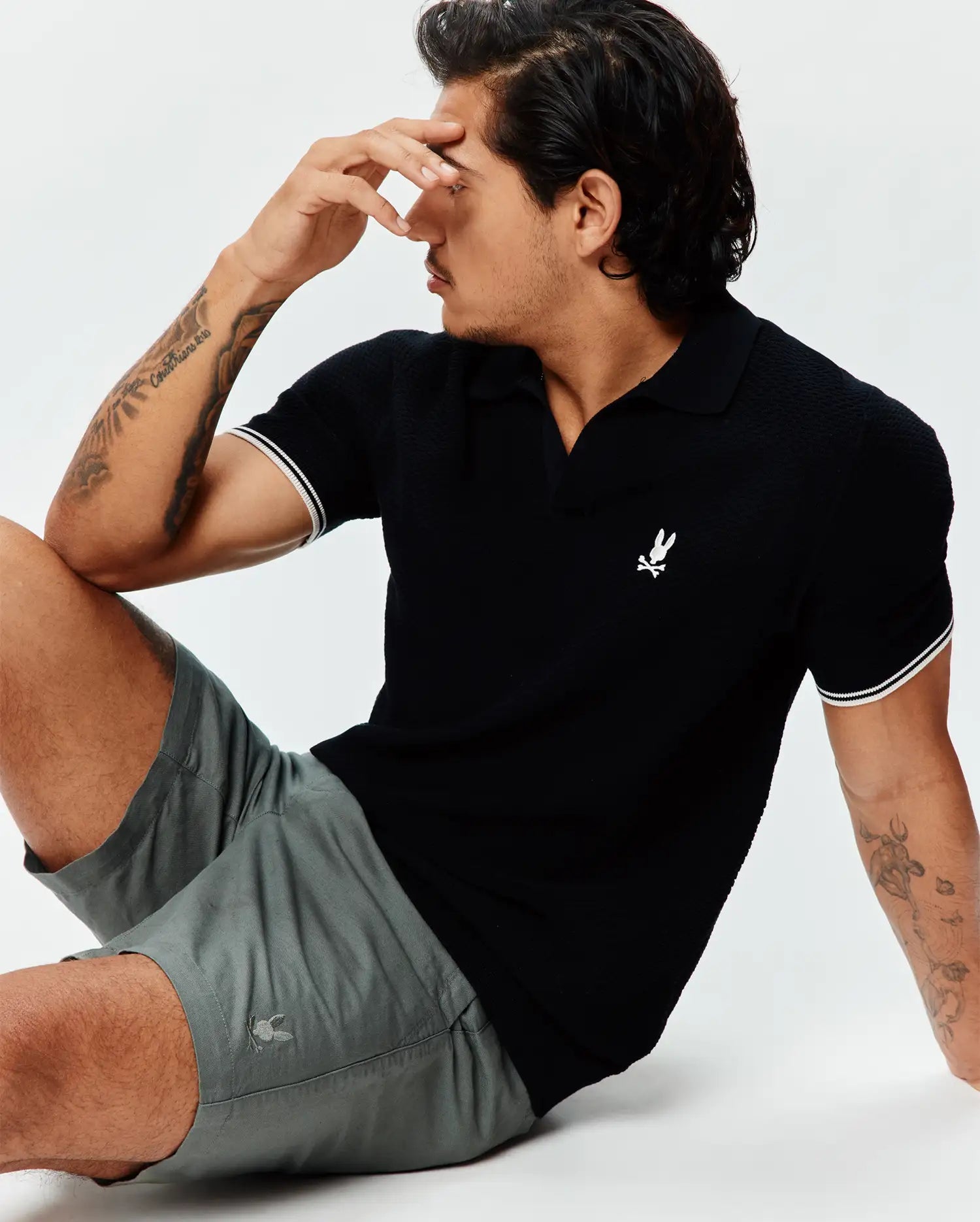 Black pique knit polo with white striped cuffs and an embroidered white Psycho Bunny logo on the chest, paired with Mens Ivan Linen Short in grey featuring a subtle embroidered grey Psycho Bunny logo on the leg.