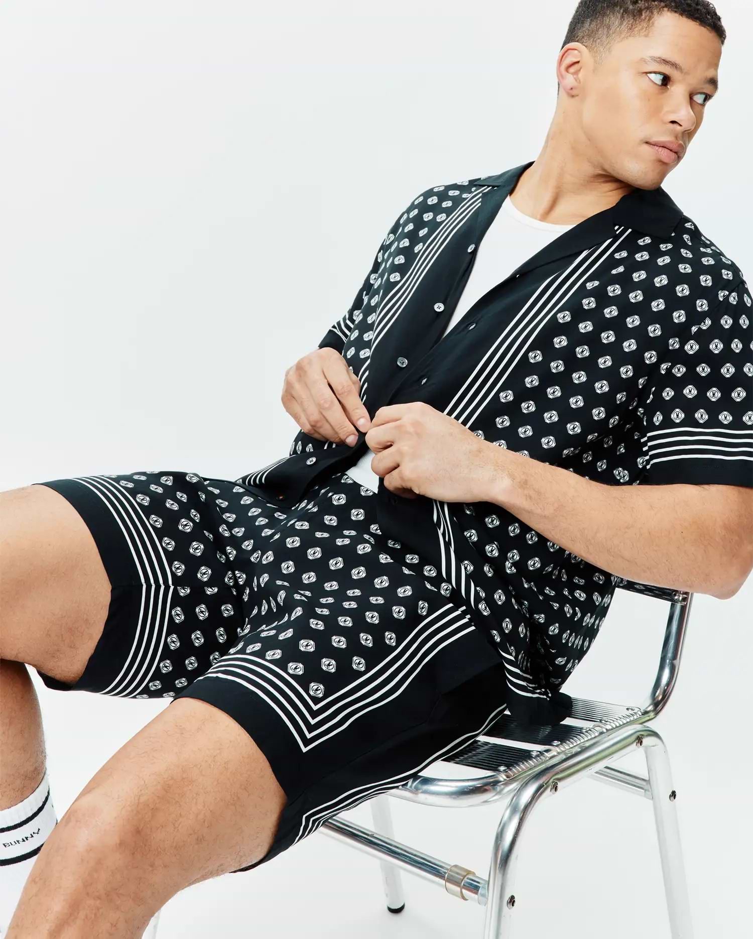 Black short-sleeve camp collar shirt and matching Mens Nick Tencel Short 7 with an all-over white Psycho Bunny skull logo pattern, featuring white stripe details on placket, cuffs, and hem.