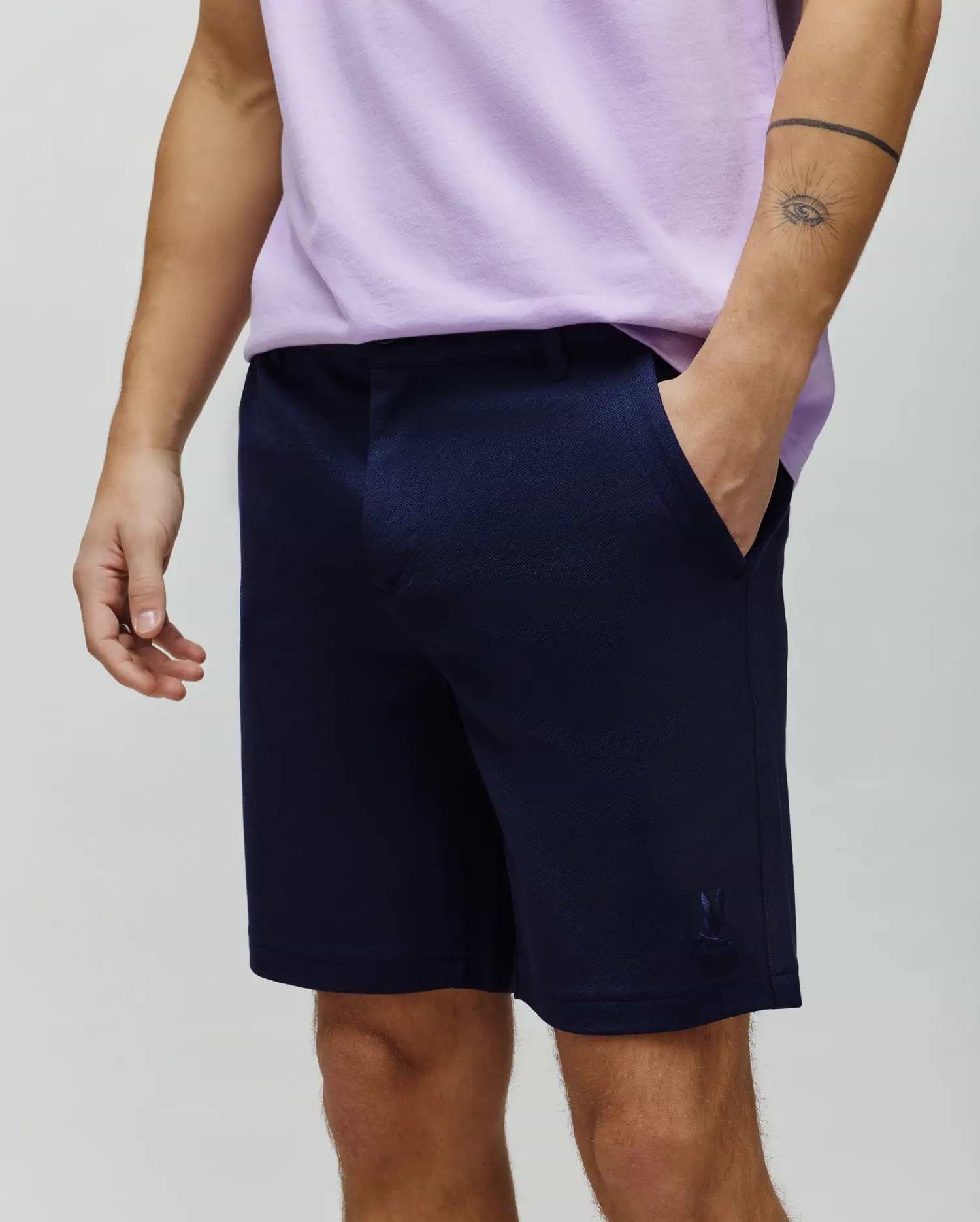 Mens Shiro Twill Short in navy blue twill fabric, featuring a subtle diagonal pattern, classic fit, and a small tonal embroidered Psycho Bunny skull logo on the lower right leg.