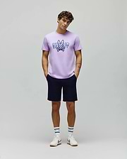 Lavender jersey t-shirt with a large distressed blue Psycho Bunny skull logo and text graphic on the chest, paired with classic fit navy MENS SHIRO TWILL SHORT.