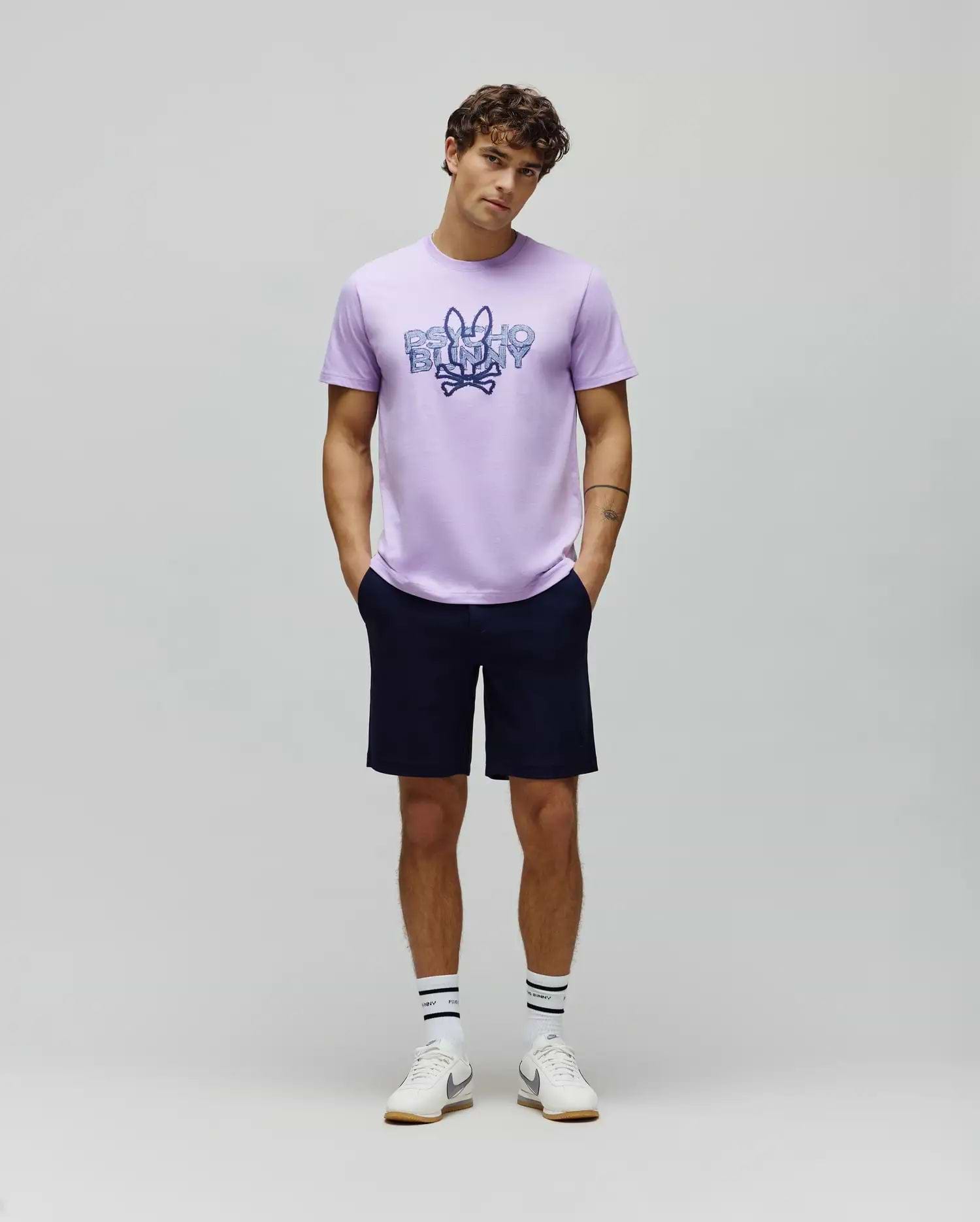 Lavender jersey t-shirt with a large distressed blue Psycho Bunny skull logo and text graphic on the chest, paired with classic fit navy MENS SHIRO TWILL SHORT.