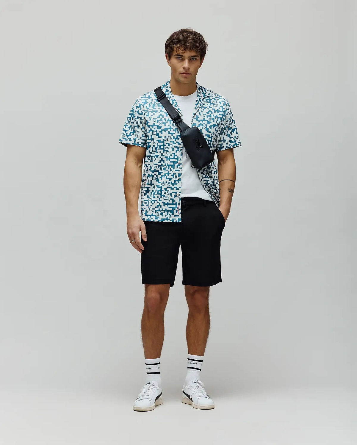 Psycho Bunny white and teal pixelated short-sleeve button-up shirt with all-over bunny skull logo pattern, layered over a white t-shirt, paired with classic fit black mens shiro twill short. (4)