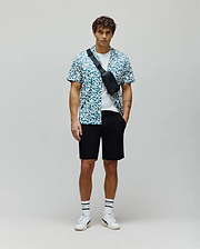 Psycho Bunny white and teal pixelated short-sleeve button-up shirt with all-over bunny skull logo pattern, layered over a white t-shirt, paired with classic fit black mens shiro twill short. (4)