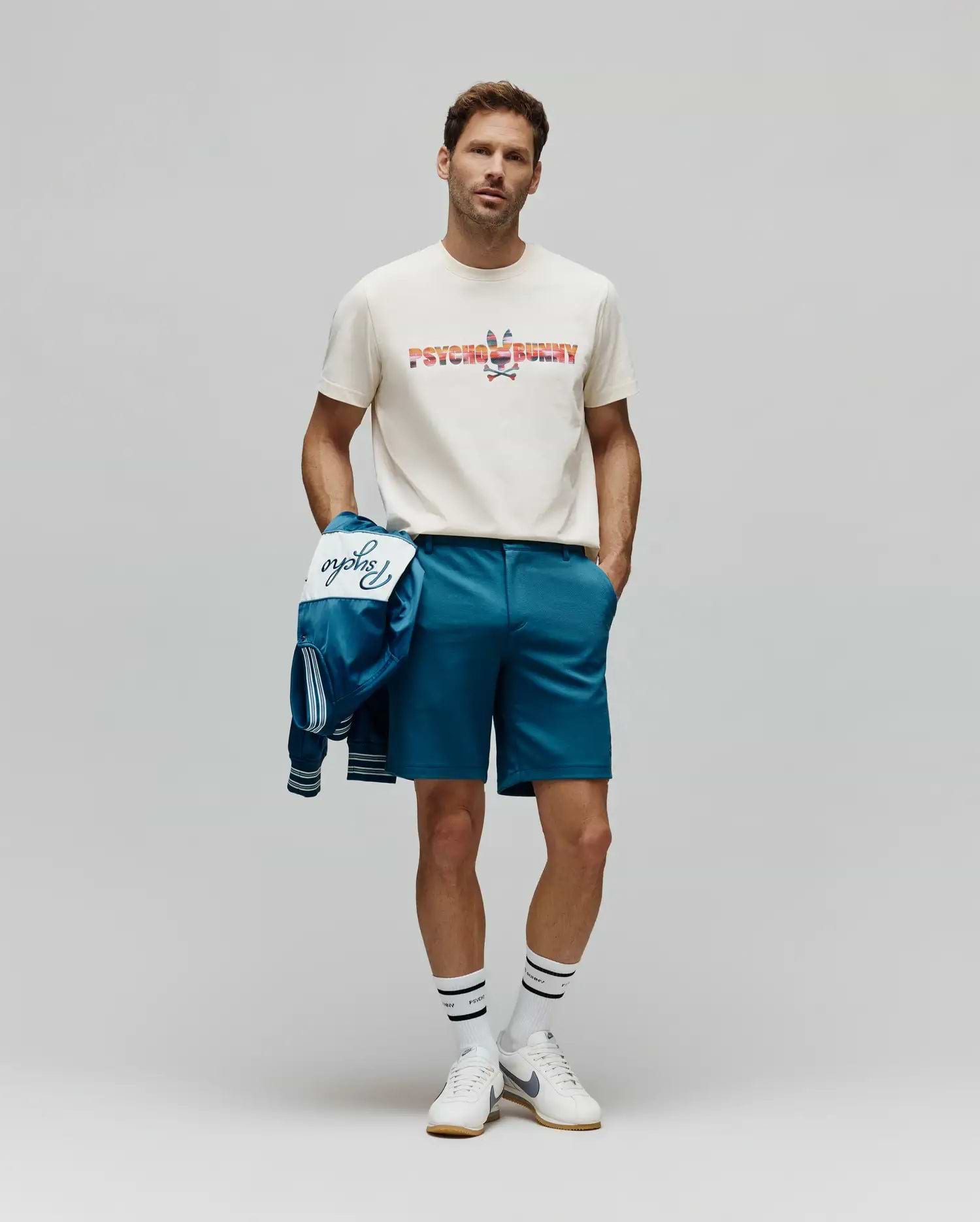 Classic fit cream jersey t-shirt featuring a large, colorful patterned Psycho Bunny logo, paired with Mens Shiro Twill Short in teal, and a matching teal bomber jacket with white Psycho script. (4)