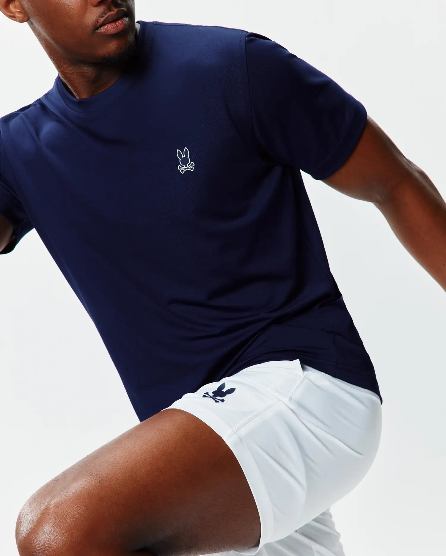 Navy performance jersey t-shirt with a small white embroidered Psycho Bunny skull logo on the left chest, paired with white Mens Blaze Sport Short featuring a navy bunny skull logo on the left leg.
