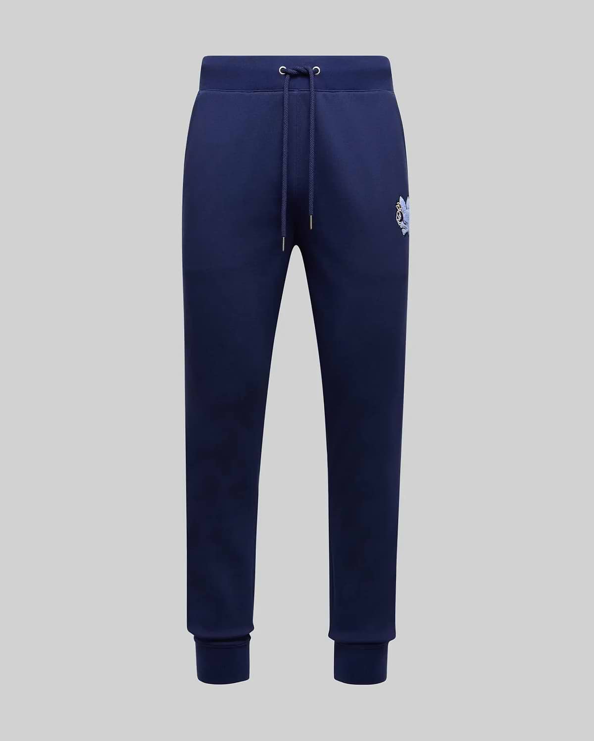 The Psycho Bunny MENS AUGUSTE JOGGER - MB0800015 in navy blue features 100% cotton, a drawstring waistband, side pockets, ribbed cuffs, and a small embroidered logo on the upper left thigh, shown on a light gray background.