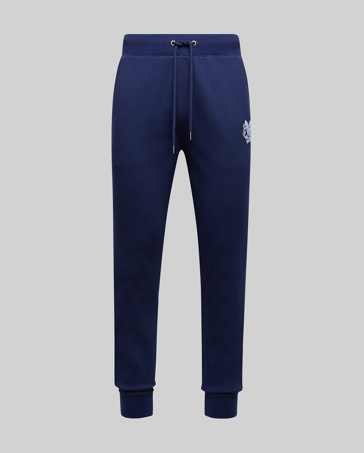 The Psycho Bunny MENS AUGUSTE JOGGER - MB0800015 in navy blue features 100% cotton, a drawstring waistband, side pockets, ribbed cuffs, and a small embroidered logo on the upper left thigh, shown on a light gray background.