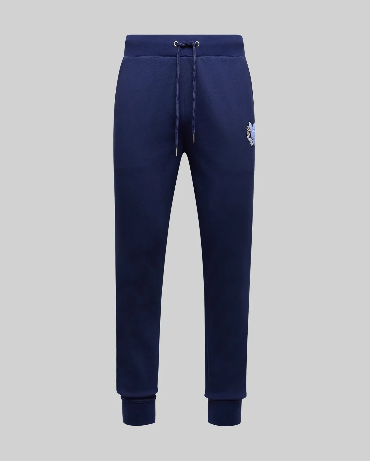 The Psycho Bunny MENS AUGUSTE JOGGER - MB0800015 in navy blue features 100% cotton, a drawstring waistband, side pockets, ribbed cuffs, and a small embroidered logo on the upper left thigh, shown on a light gray background.