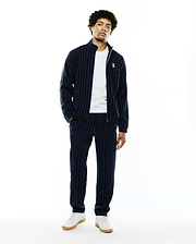 Mens Harland Double Weave Chalk Stripe Track Pant and matching full-zip jacket. Navy blue relaxed fit tracksuit with white pinstripes, green sleeve stripe, and embroidered Psycho Bunny skull logo. (1)