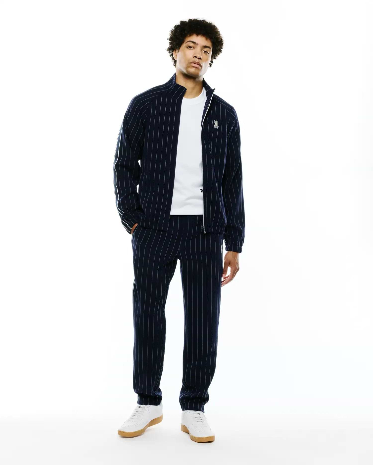 Mens Harland Double Weave Chalk Stripe Track Pant and matching full-zip jacket. Navy blue relaxed fit tracksuit with white pinstripes, green sleeve stripe, and embroidered Psycho Bunny skull logo. (1)