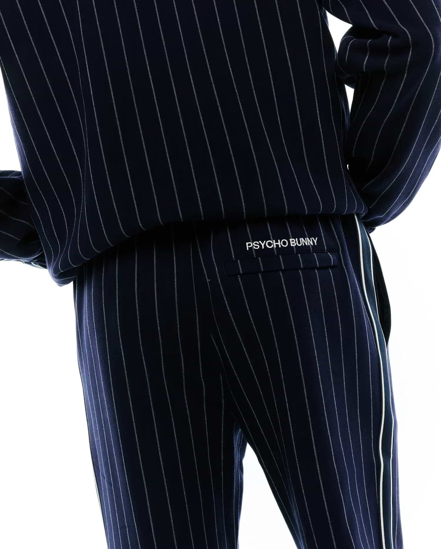 Mens Harland Double Weave Chalk Stripe Track Pant, navy with fine white pinstripes, a relaxed fit, and a prominent white side stripe. White embroidered PSYCHO BUNNY branding is on the back flap pocket. (4)
