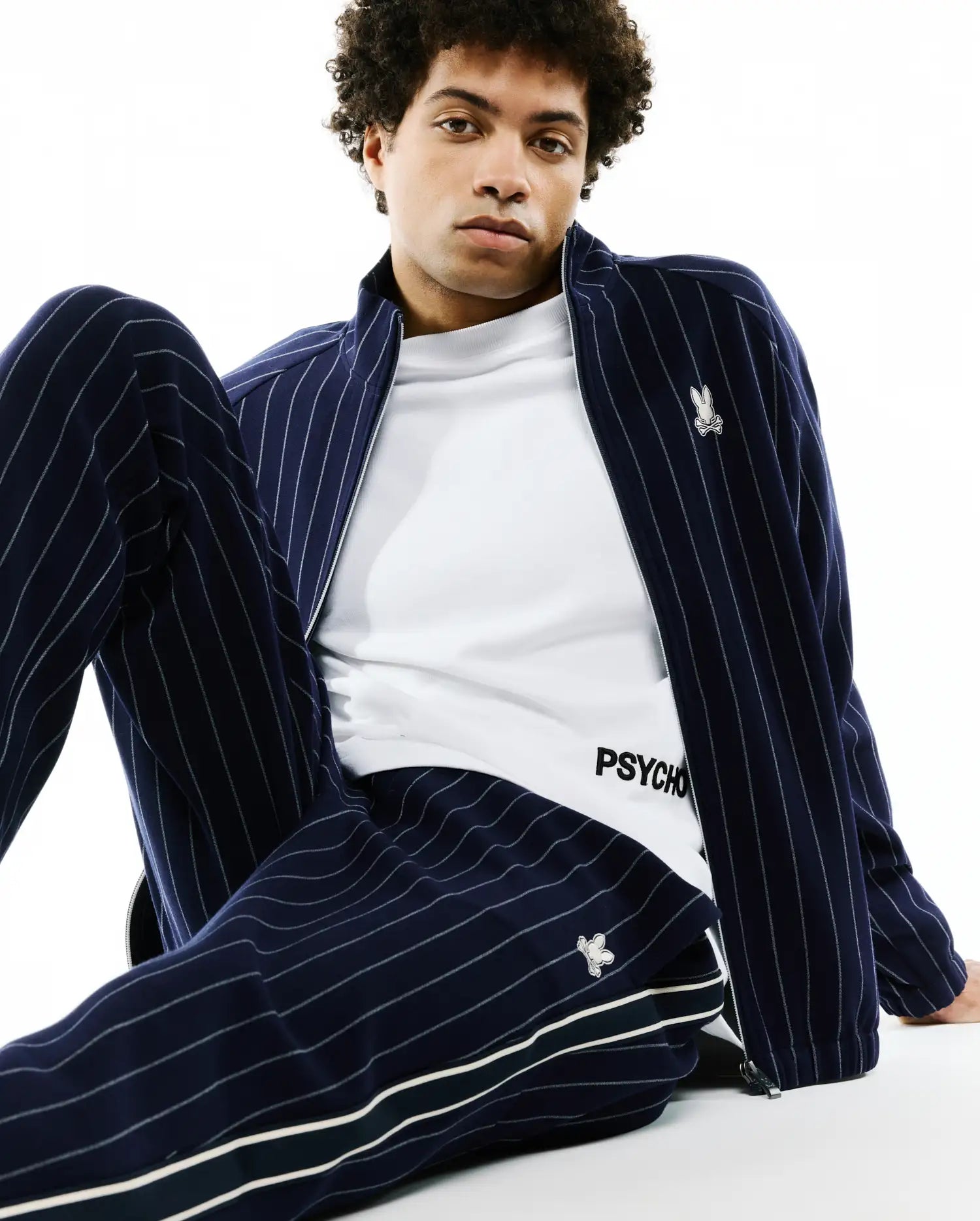 Navy blue chalk stripe track jacket with embroidered bunny skull logo on chest, matching Mens Harland Double Weave Chalk Stripe Track Pant with side stripes and logo, over a white PSYCHO t-shirt. (3)