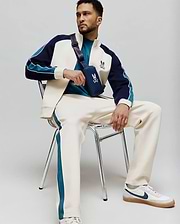 Cream MENS CASPIAN TRACK PANT with teal side stripes, paired with a cream, navy, and teal color-block track jacket featuring an embroidered Psycho Bunny logo, and a teal t-shirt. (4)