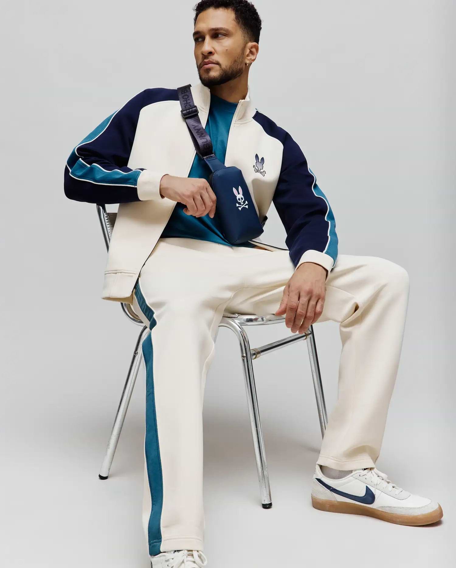Cream MENS CASPIAN TRACK PANT with teal side stripes, paired with a cream, navy, and teal color-block track jacket featuring an embroidered Psycho Bunny logo, and a teal t-shirt. (4)