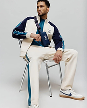 Cream MENS CASPIAN TRACK PANT with teal side stripes, paired with a cream, navy, and teal color-block track jacket featuring an embroidered Psycho Bunny logo, and a teal t-shirt. (4)