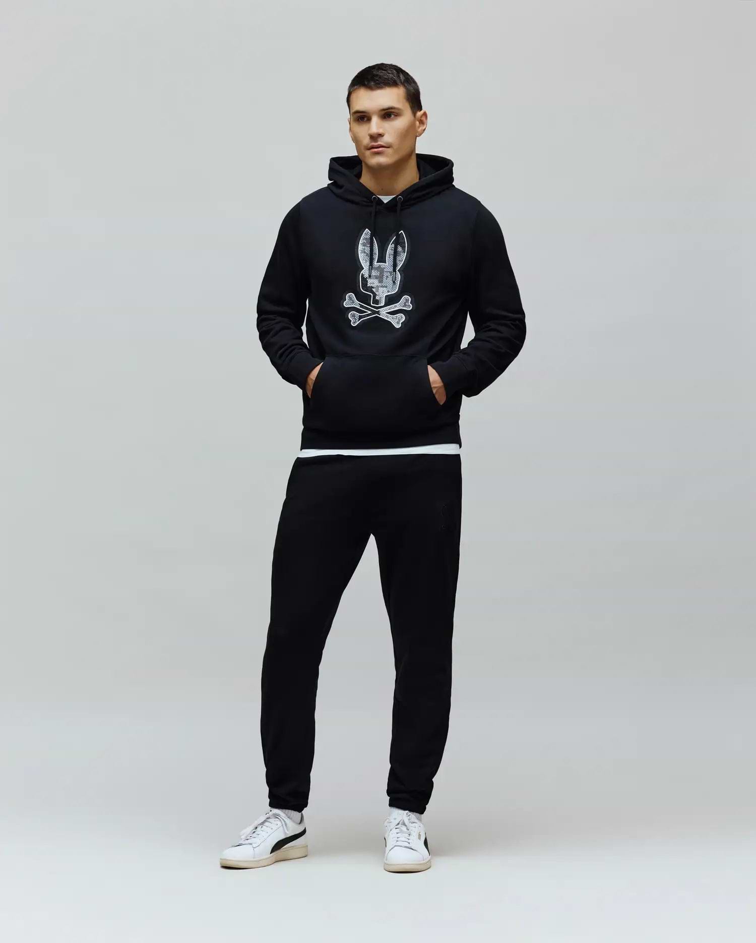 Black classic fit French terry hoodie with a large distressed white Psycho Bunny skull logo on the chest, paired with black slim Mens Barry Joggers featuring a small embroidered bunny logo.
