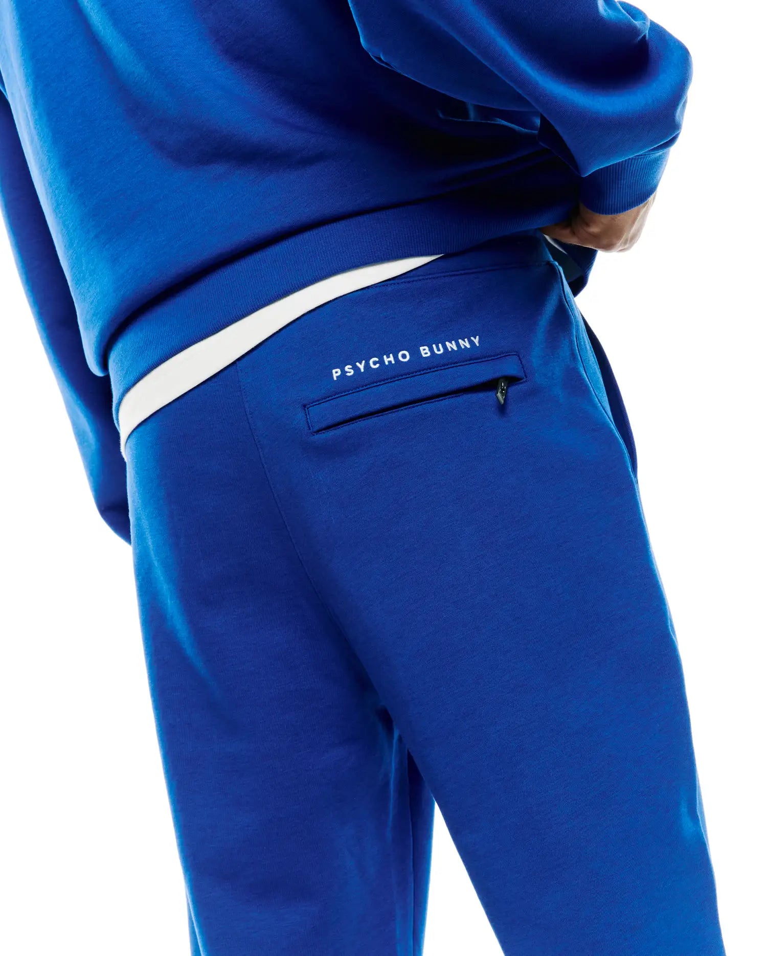 Royal blue Mens Nathaniel Sweatpant, a relaxed fit french terry garment, features a white Psycho Bunny text logo above a zippered back pocket and a contrasting white waistband. (3)