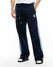 Mens Jaydon Track Pant in navy, featuring a relaxed fit, smooth knit fabric, drawstring waist, and a small embroidered white Psycho Bunny skull logo on the left thigh, with light blue gradient vertical stripes on the sides. (1)