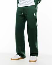 Mens Jaydon Track Pant in dark green, featuring a relaxed wide leg fit, smooth knit fabric, drawstring waist with white tips, and a small embroidered white Psycho Bunny skull logo on the left hip. (3)