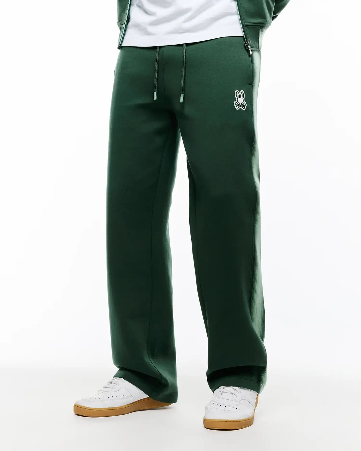 Mens Jaydon Track Pant in dark green, featuring a relaxed wide leg fit, smooth knit fabric, drawstring waist with white tips, and a small embroidered white Psycho Bunny skull logo on the left hip. (3)