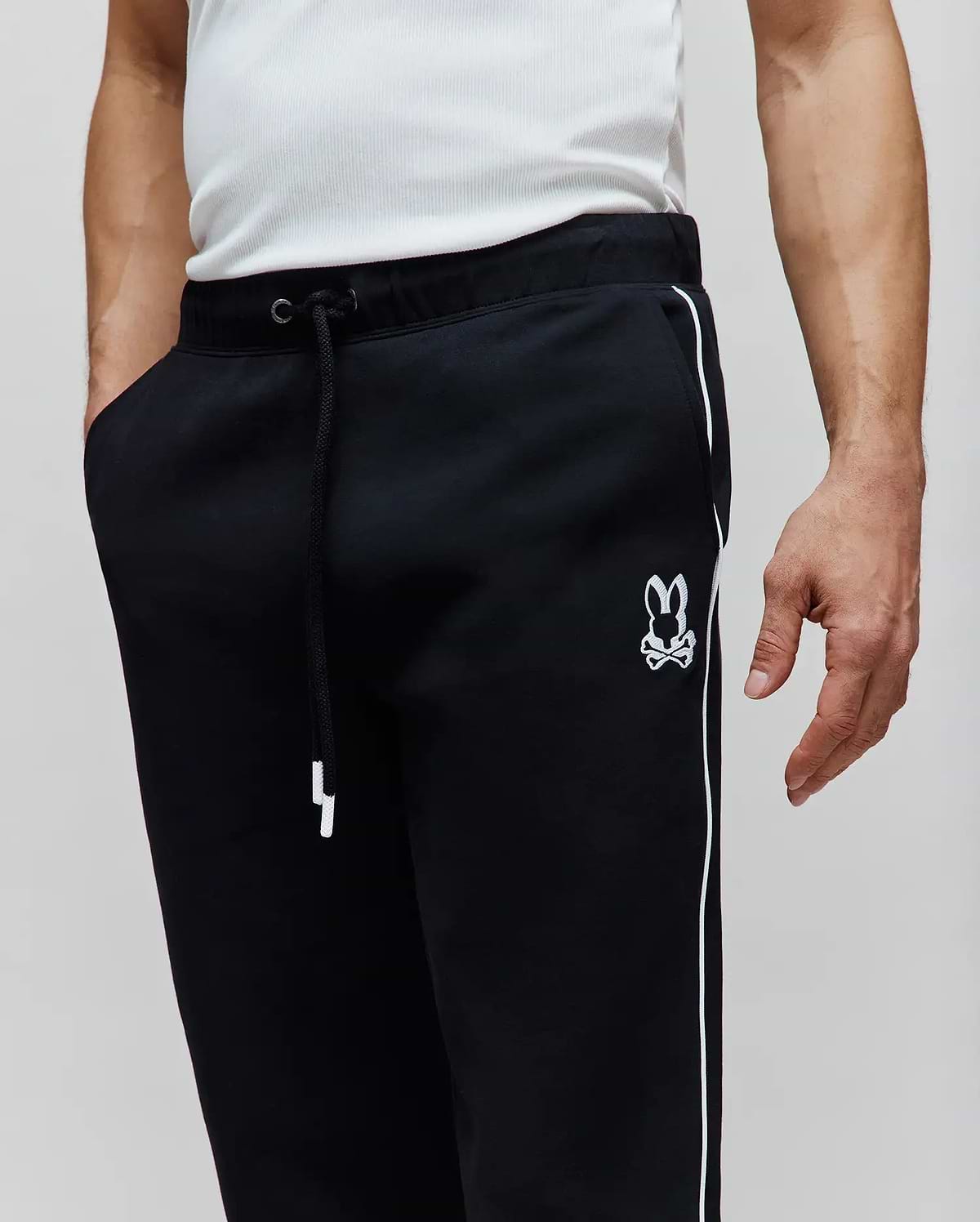 Mens Toby Track Pants, black relaxed fit French terry with white side stripes, white drawstring, and an embroidered white Psycho Bunny skull logo on the left thigh.