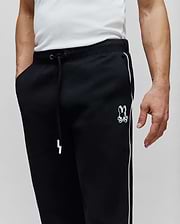 Mens Toby Track Pants, black relaxed fit French terry with white side stripes, white drawstring, and an embroidered white Psycho Bunny skull logo on the left thigh.