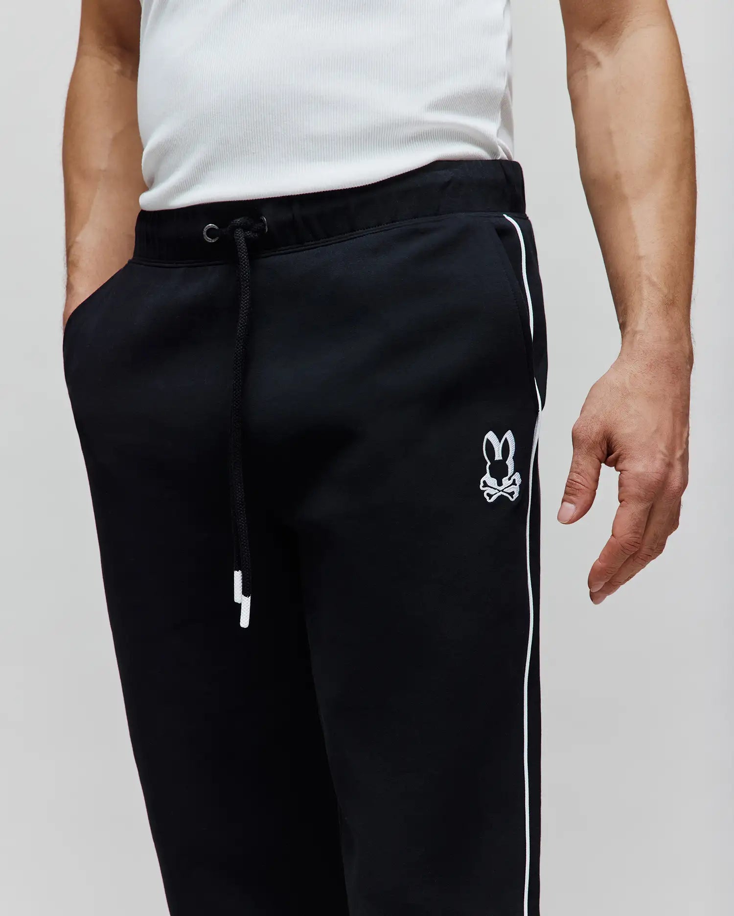Mens Toby Track Pants, black relaxed fit French terry with white side stripes, white drawstring, and an embroidered white Psycho Bunny skull logo on the left thigh.