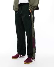 Deep green crinkled nylon Alder Nylon Colorblock Pant with a relaxed fit, featuring olive green and burgundy side stripes and a small white embroidered Psycho Bunny skull logo on the left thigh.