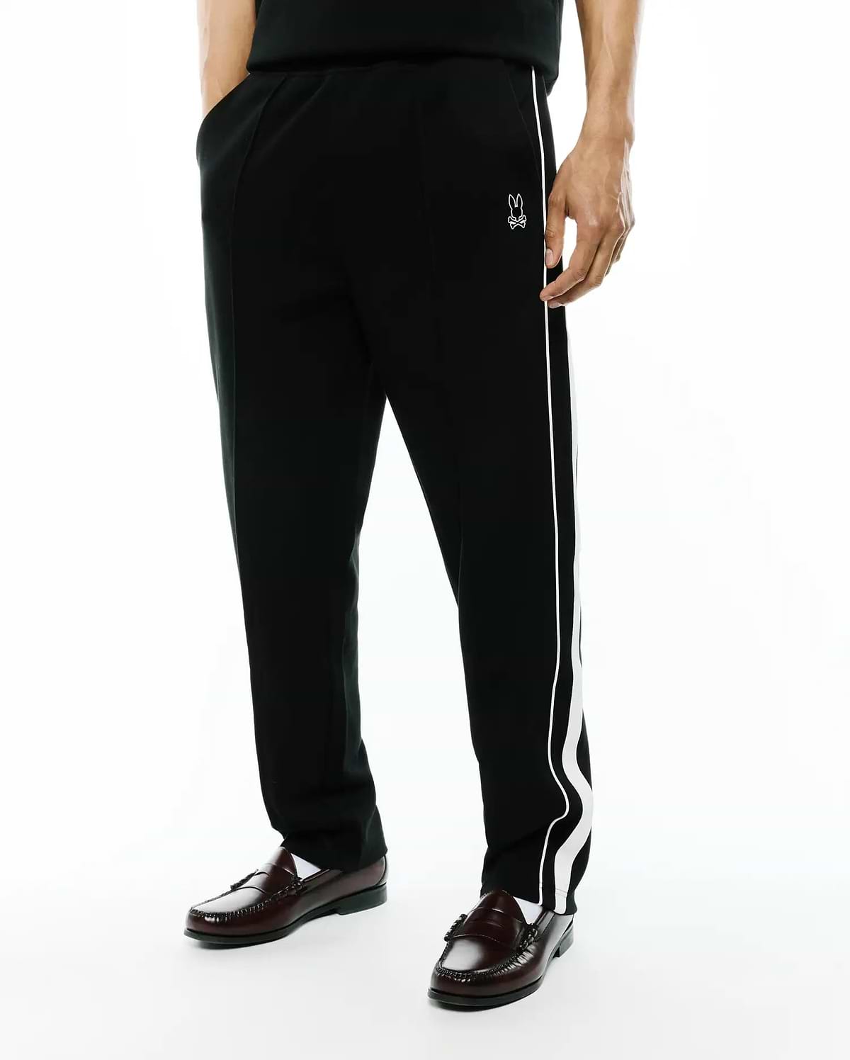Black Mens Ceano Track Pant, relaxed fit, smooth knit, with a distinctive white wavy side stripe and a small embroidered white Psycho Bunny skull logo on the left hip.