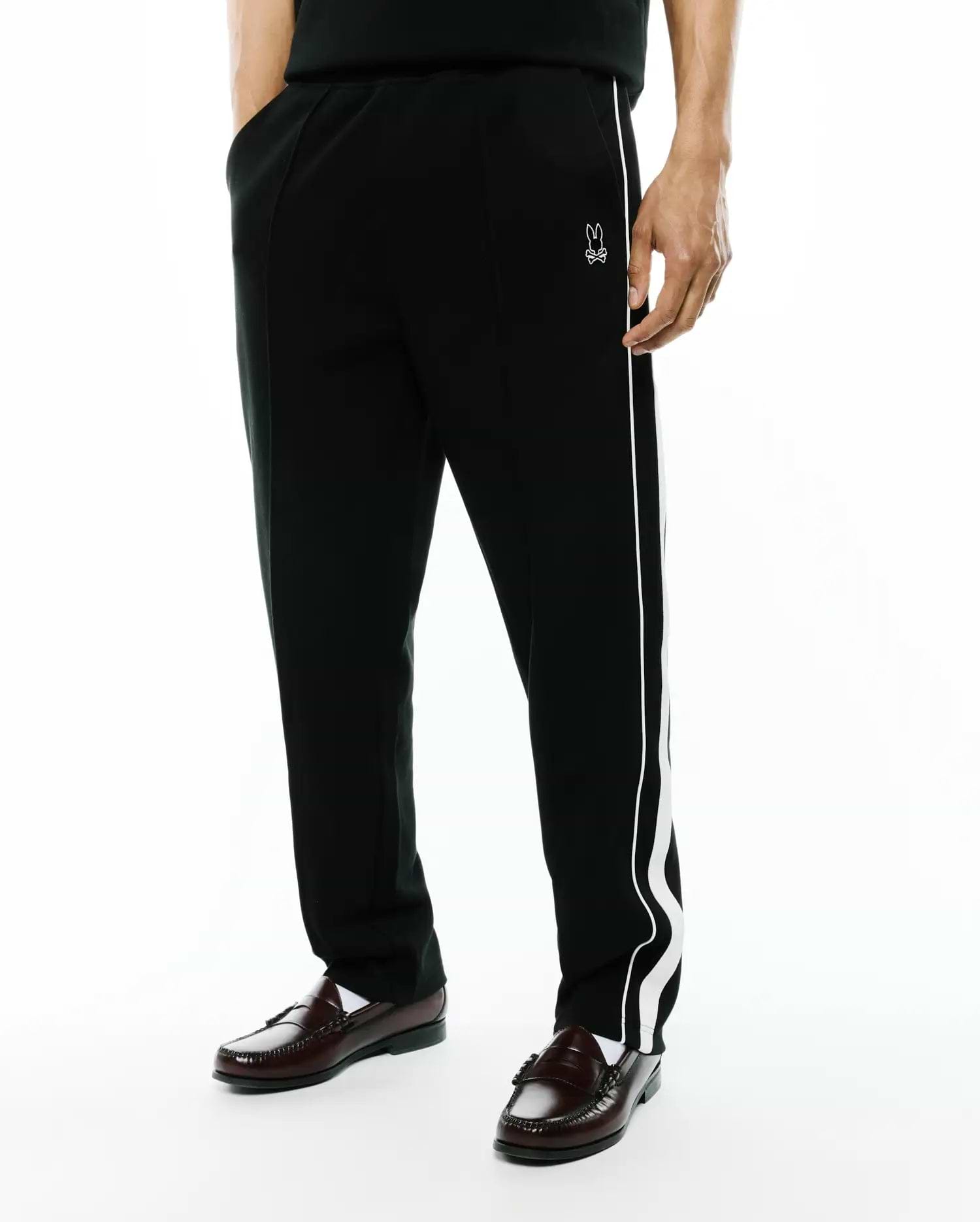Black Mens Ceano Track Pant, relaxed fit, smooth knit, with a distinctive white wavy side stripe and a small embroidered white Psycho Bunny skull logo on the left hip.