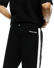 Mens Ceano Track Pant, black smooth knit with a white side stripe, featuring a white Psycho Bunny skull tag on the back waist and embroidered PSYCHO BUNNY text above the back pocket.
