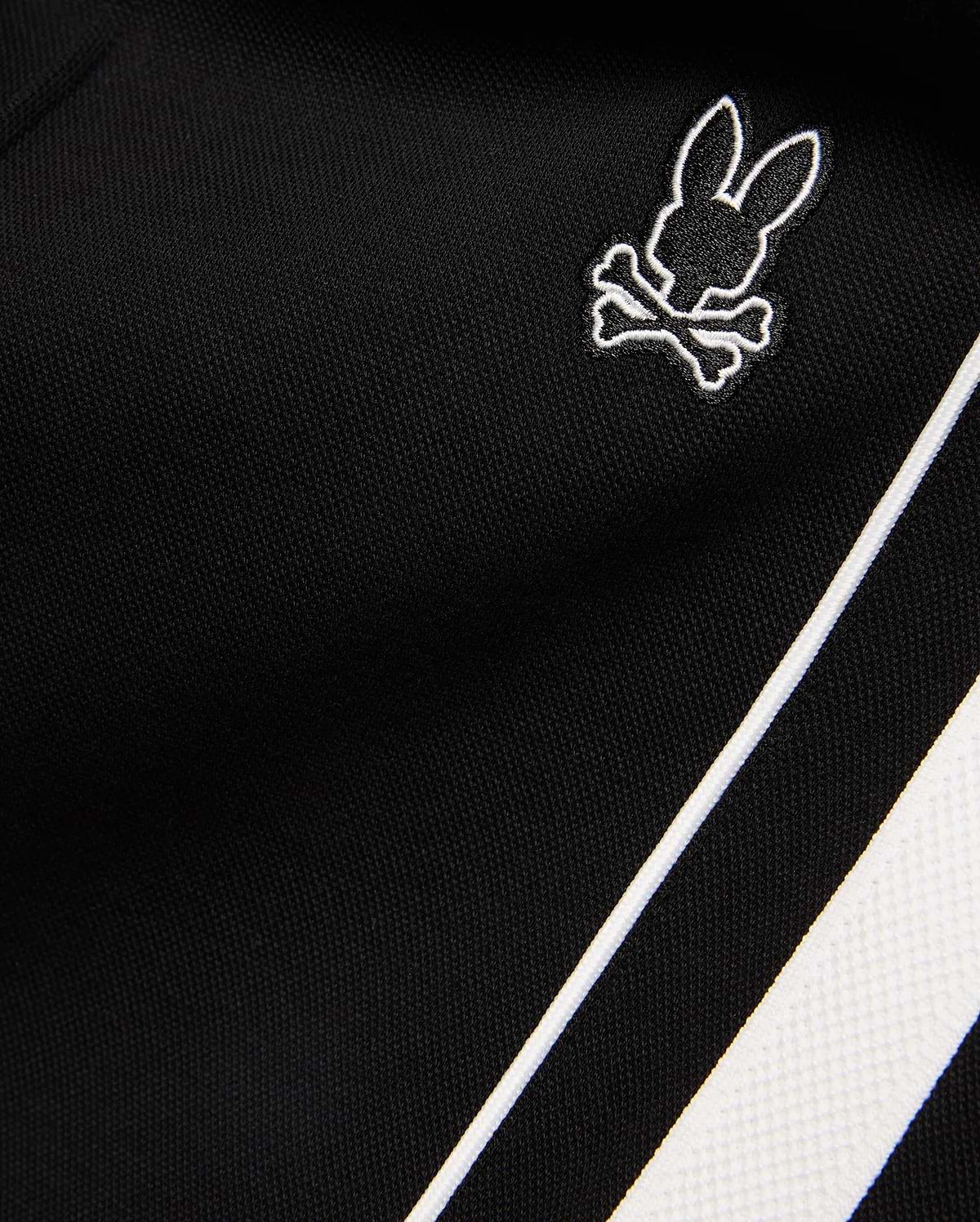 Mens Ceano Track Pant in black smooth knit fabric, featuring a small embroidered white outline Psycho Bunny skull logo and a bold white side stripe with piping.