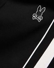 Mens Ceano Track Pant in black smooth knit fabric, featuring a small embroidered white outline Psycho Bunny skull logo and a bold white side stripe with piping.