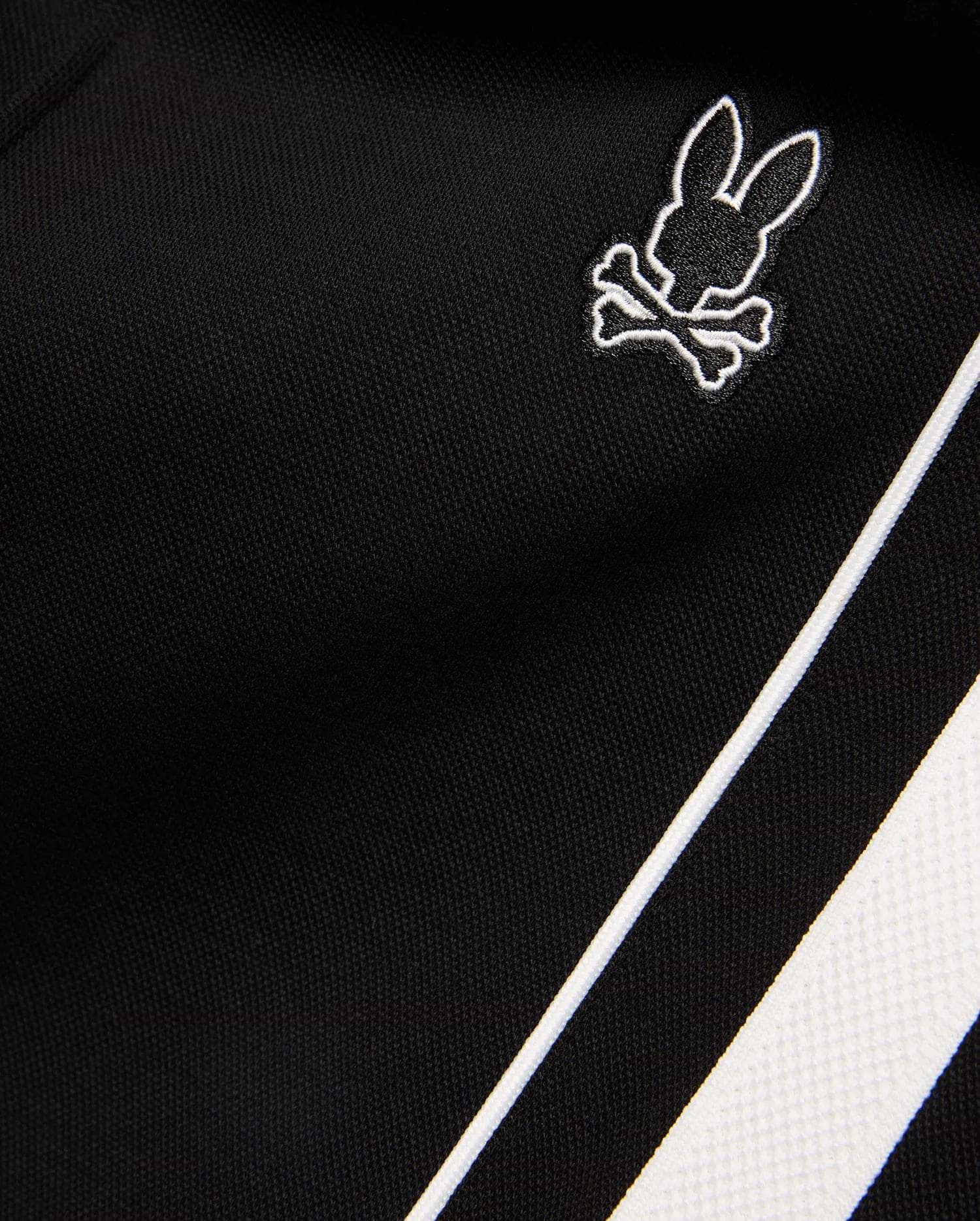 Mens Ceano Track Pant in black smooth knit fabric, featuring a small embroidered white outline Psycho Bunny skull logo and a bold white side stripe with piping.