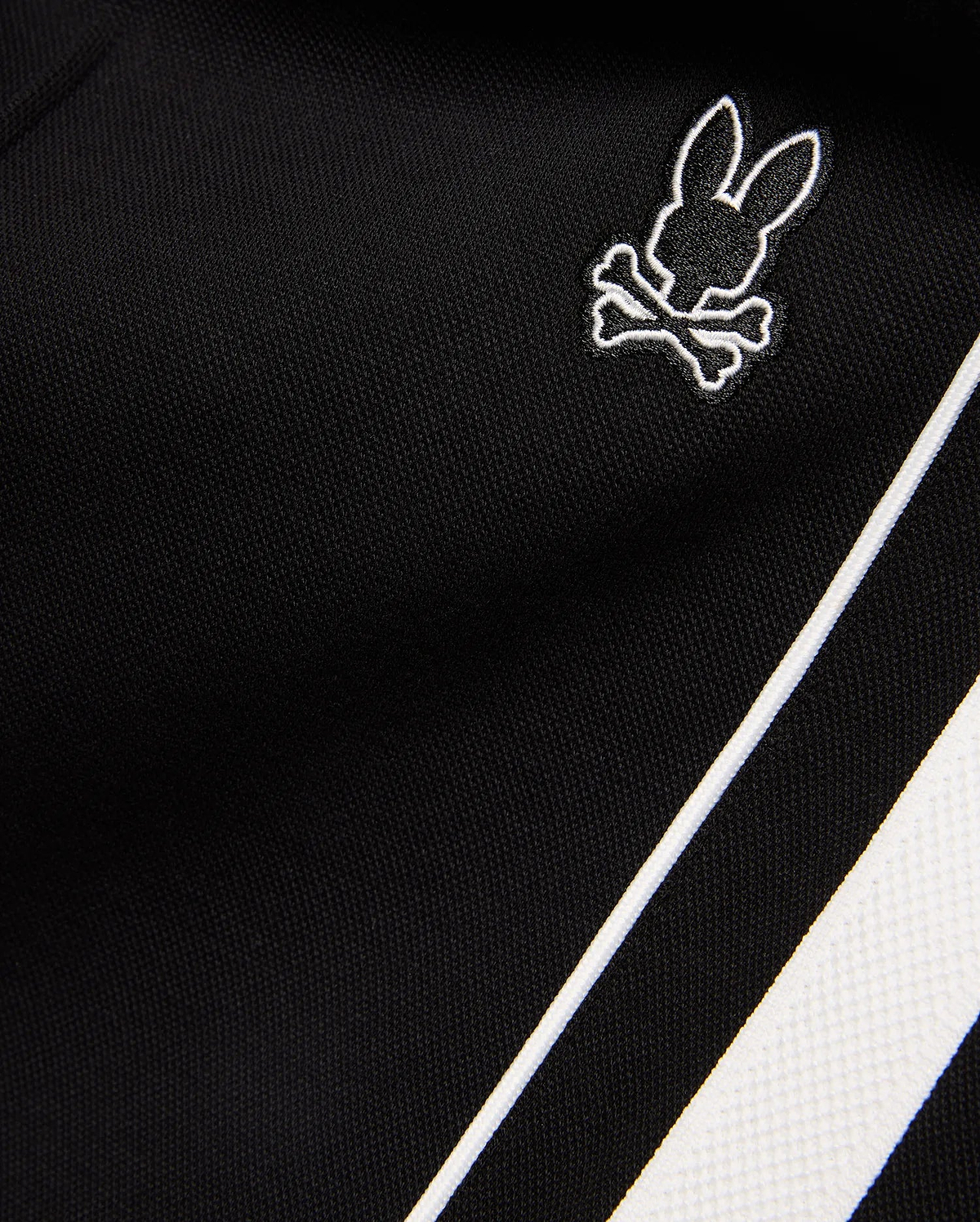 Mens Ceano Track Pant in black smooth knit fabric, featuring a small embroidered white outline Psycho Bunny skull logo and a bold white side stripe with piping.