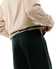 Dark charcoal Mens Terrence Brushed Fleece Sweatpant featuring a relaxed fit, elastic waistband, side pockets, and a subtle zippered back pocket, paired with a beige long-sleeve top.