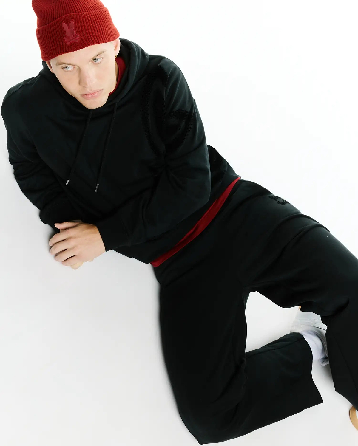 Red ribbed Psycho Bunny beanie with tonal skull logo, black classic fit French terry hoodie with red drawstring and subtle sleeve logo, paired with black Men's Johan Straight-Leg Sweatpants. (4)