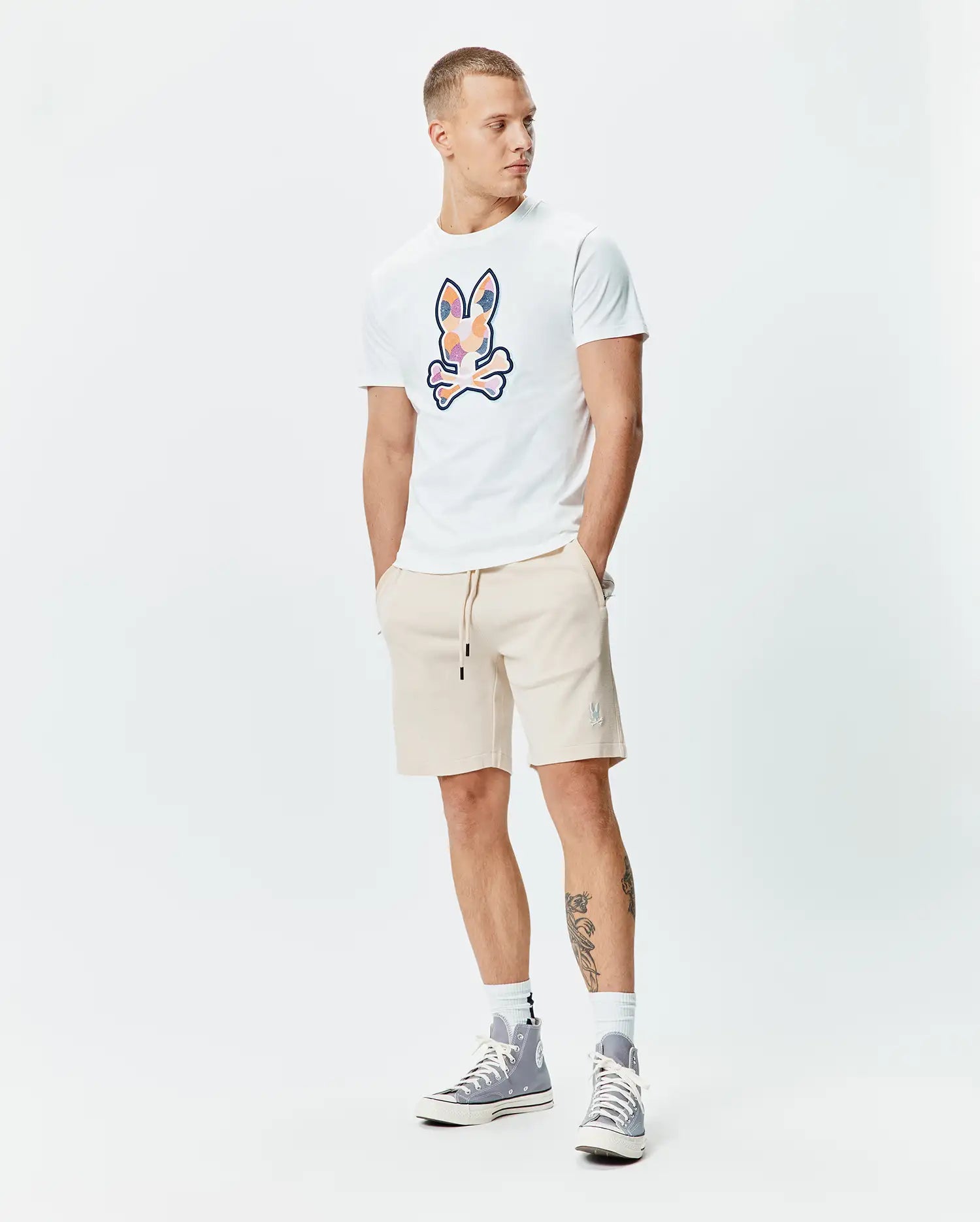 White jersey t-shirt with large colorful graphic Psycho Bunny skull chest logo. Beige French terry Mens Keith Short 8, featuring black drawstrings and small embroidered Psycho Bunny thigh logo.