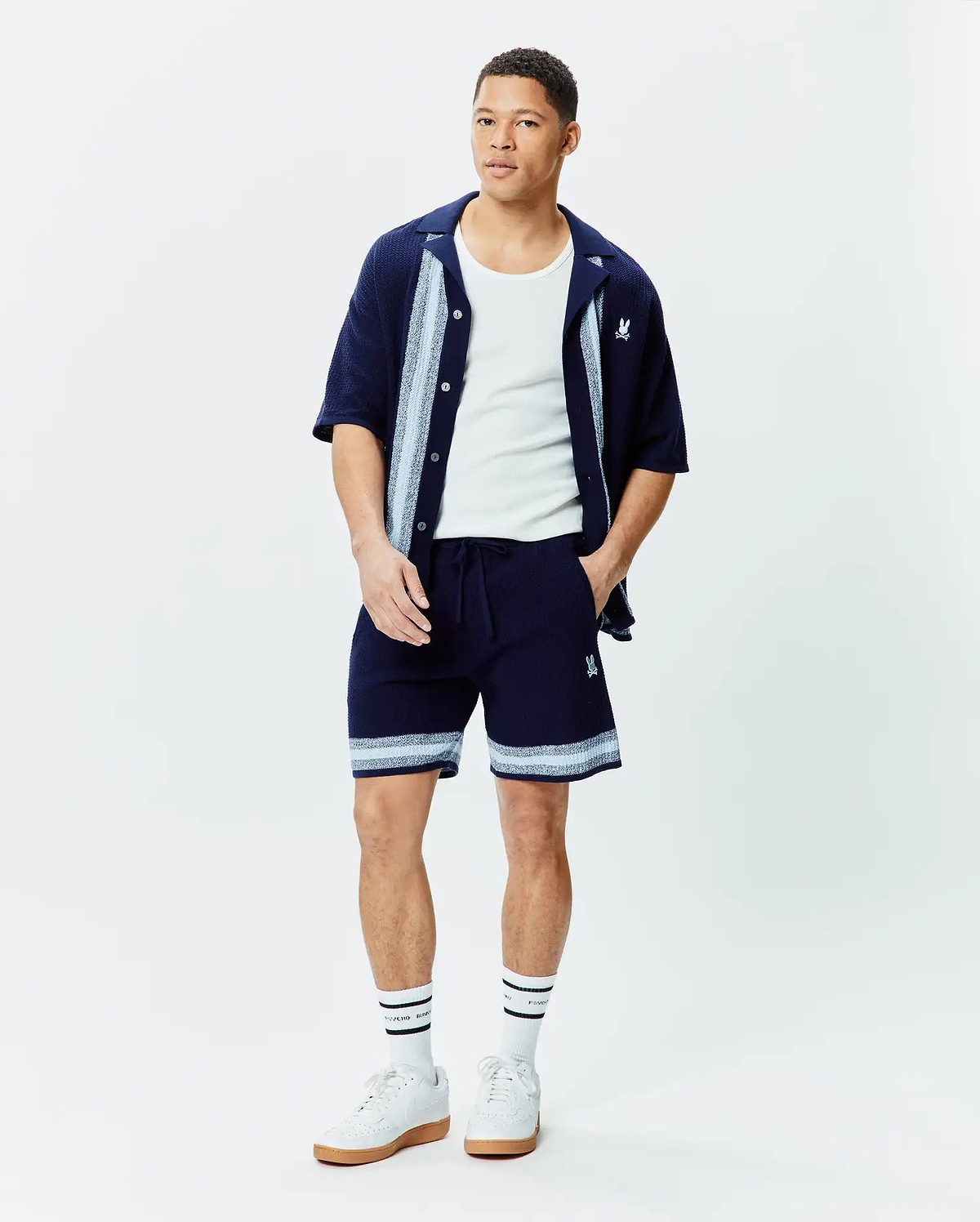 Navy Mens Giles Knit Short 7, relaxed fit, with light blue and white striped knit hem and embroidered Psycho Bunny skull, paired with a matching navy knit short-sleeve shirt with striped placket and chest logo.