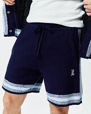 Mens Giles Knit Short 7. Navy blue textured knit shorts with a drawstring waist, light blue and white striped hem, side panel, and small embroidered Psycho Bunny logo on the right leg.