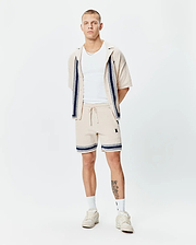 Mens Giles Knit Short 7 and matching collared shirt in beige textured knit with navy and white striped accents and small embroidered Psycho Bunny skull logo on shorts' thigh.