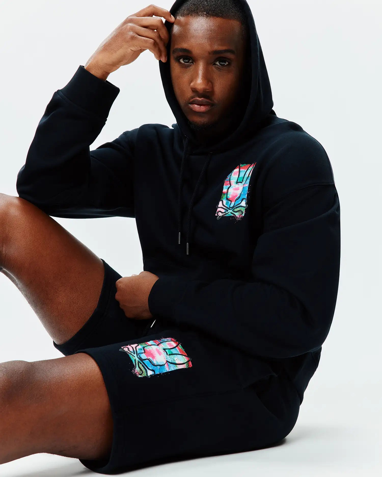 Black relaxed fit hoodie and Mens Isaac Print Short, both in soft jersey, featuring a vibrant multi-color Psycho Bunny skull logo on the left chest and left thigh.
