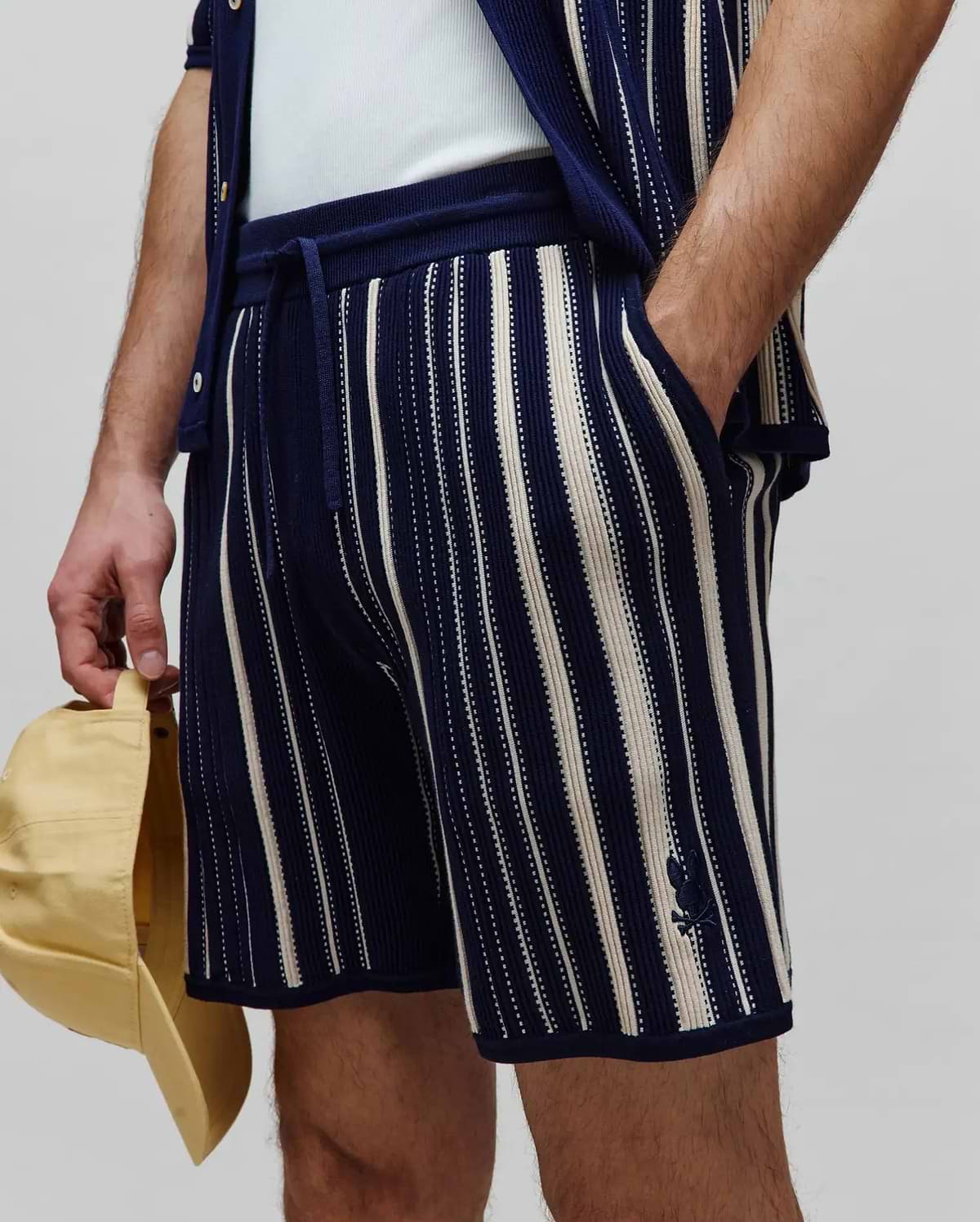 Mens Cliff Knit Short: Relaxed fit navy knit shorts with cream vertical stripes, featuring a drawstring waist and a small embroidered Psycho Bunny skull logo on the left leg.