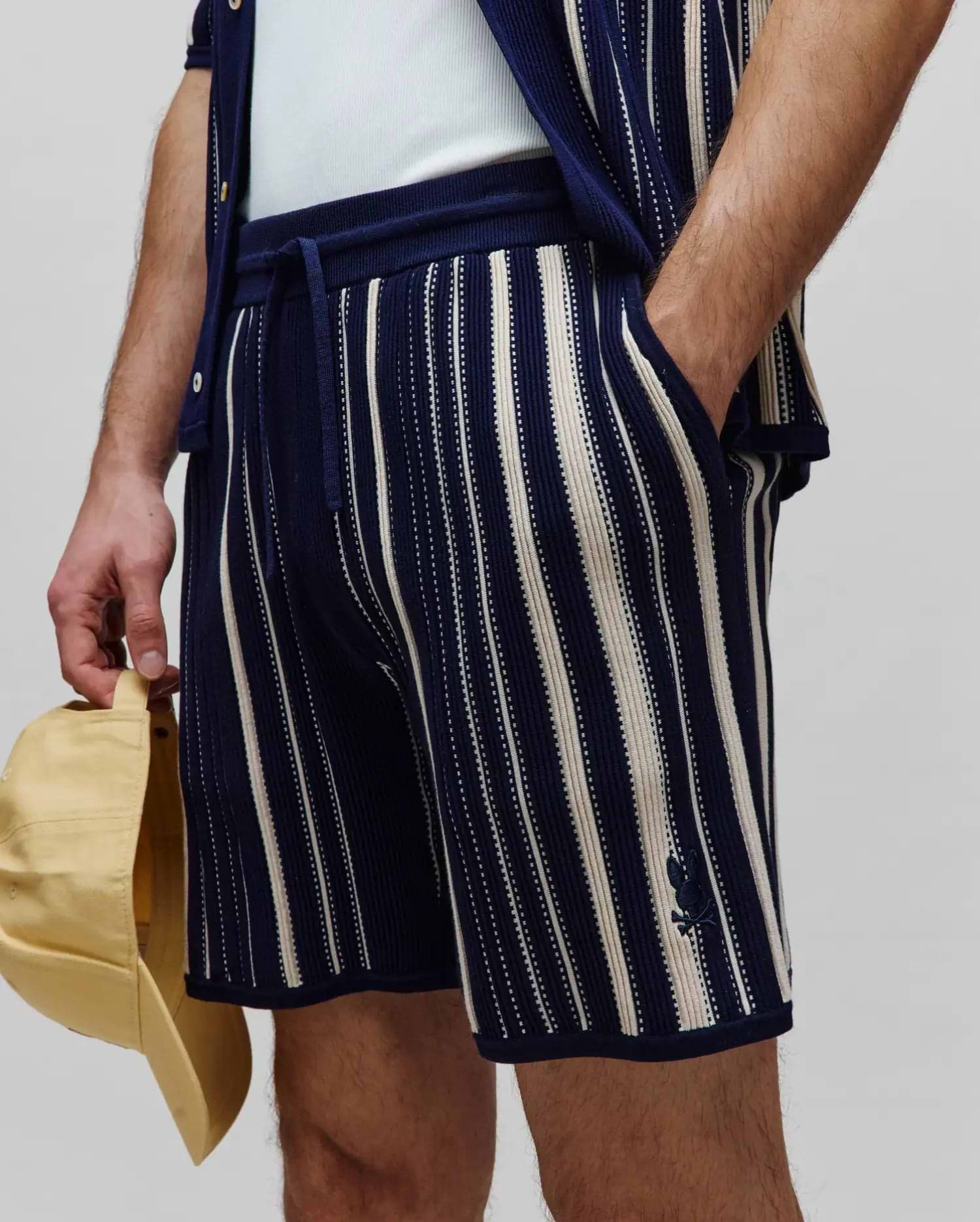 Mens Cliff Knit Short: Relaxed fit navy knit shorts with cream vertical stripes, featuring a drawstring waist and a small embroidered Psycho Bunny skull logo on the left leg.
