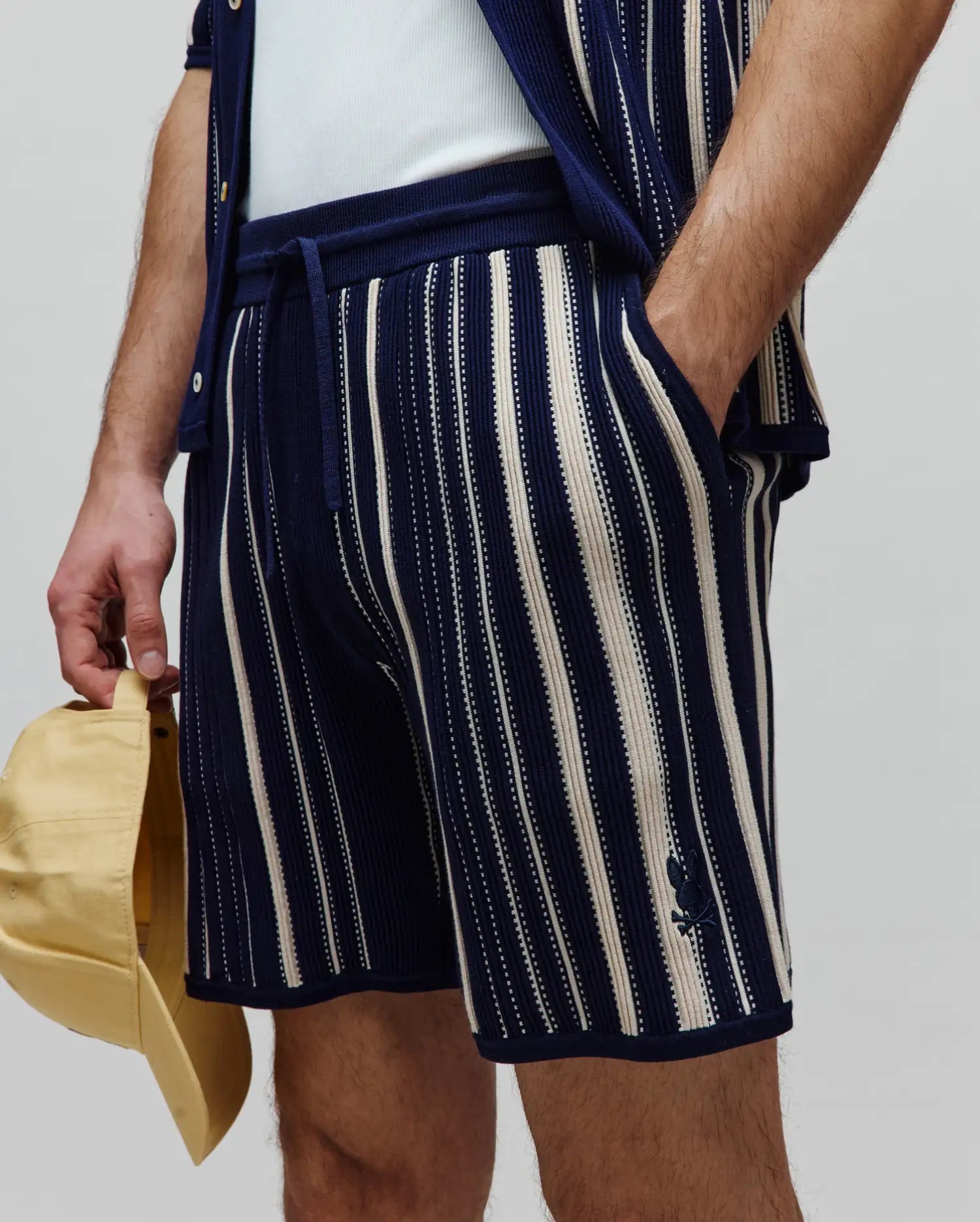 Mens Cliff Knit Short: Relaxed fit navy knit shorts with cream vertical stripes, featuring a drawstring waist and a small embroidered Psycho Bunny skull logo on the left leg.