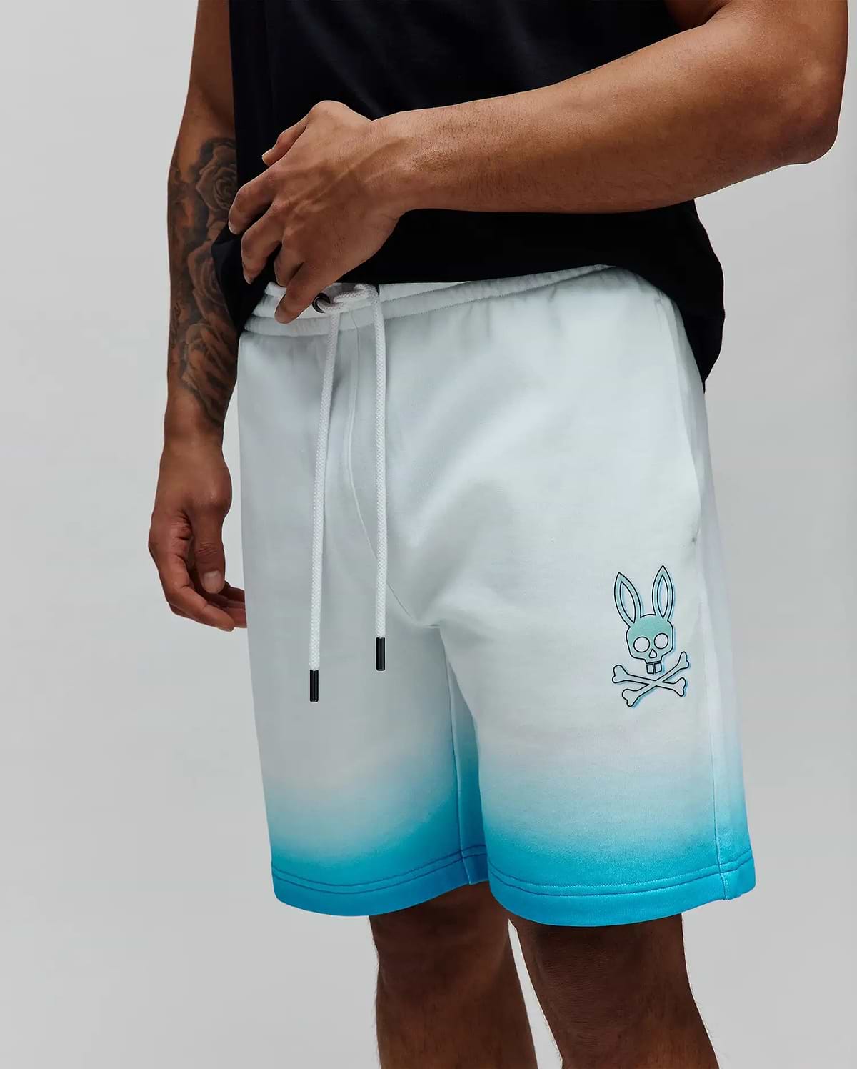 Mens Dax Sweatshort in a white to vibrant blue ombre fade, featuring a relaxed fit, soft French terry fabric, and a prominent light blue Psycho Bunny skull and crossbones logo on the left thigh. (2)