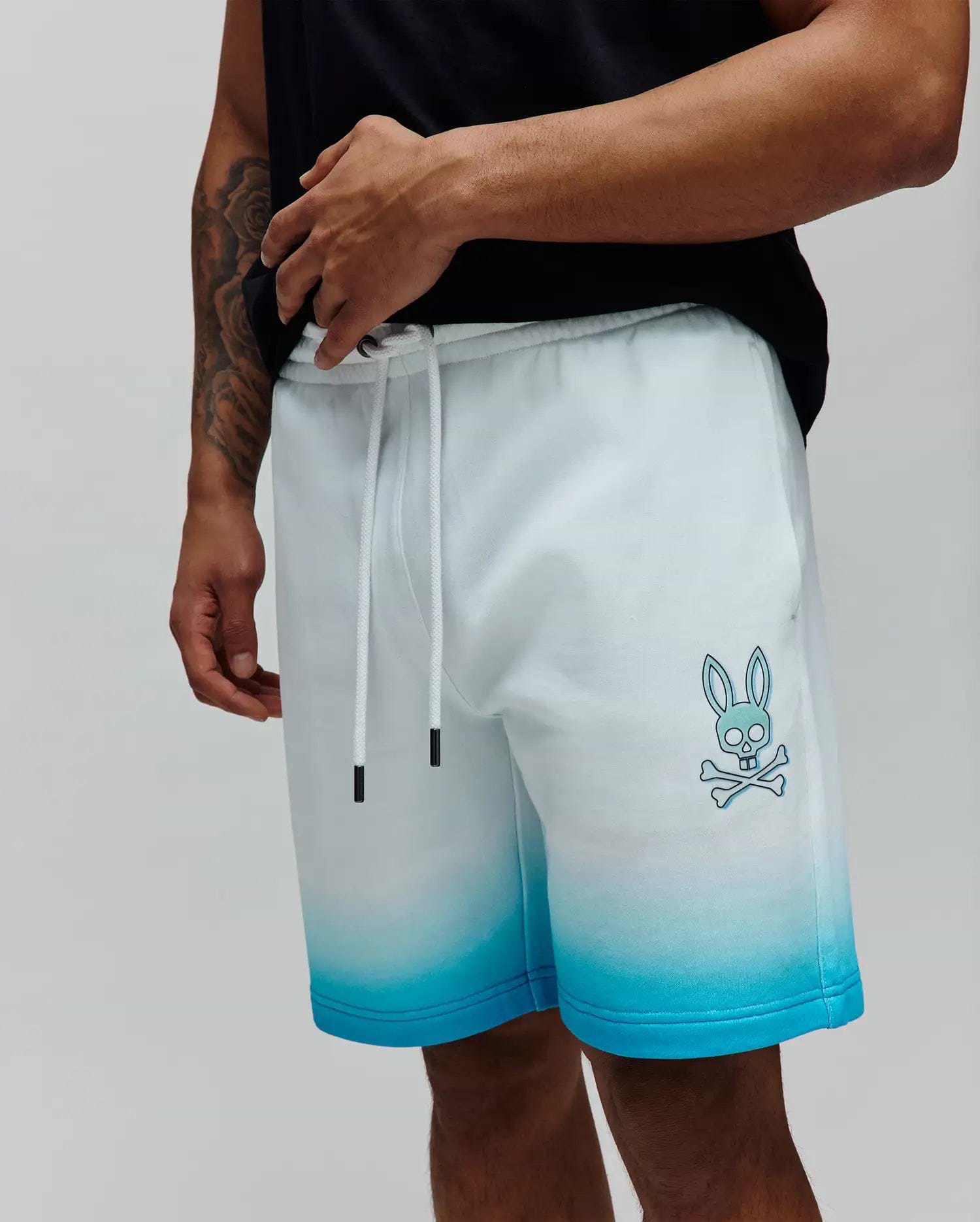 Mens Dax Sweatshort in a white to vibrant blue ombre fade, featuring a relaxed fit, soft French terry fabric, and a prominent light blue Psycho Bunny skull and crossbones logo on the left thigh. (2)
