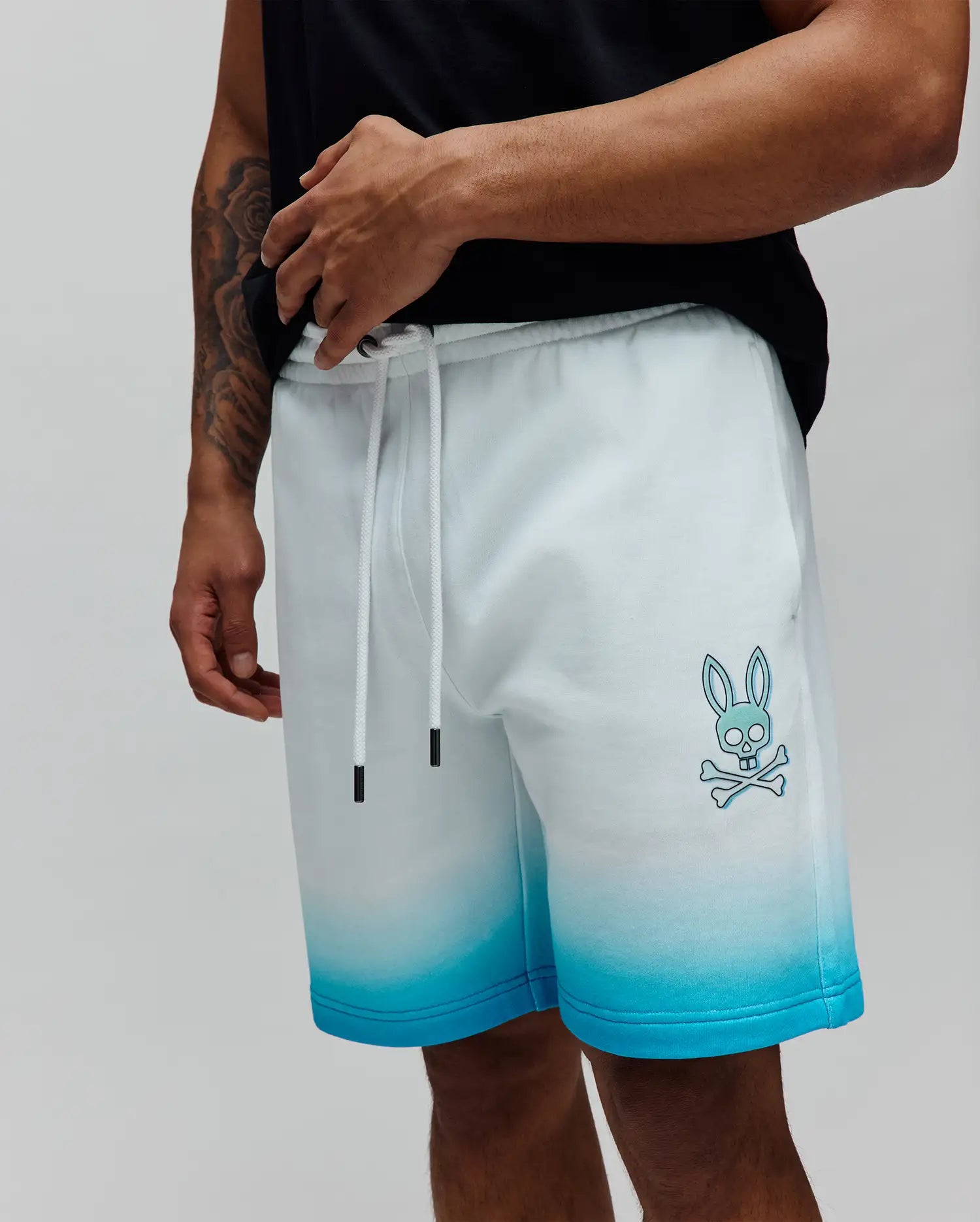 Mens Dax Sweatshort in a white to vibrant blue ombre fade, featuring a relaxed fit, soft French terry fabric, and a prominent light blue Psycho Bunny skull and crossbones logo on the left thigh. (2)
