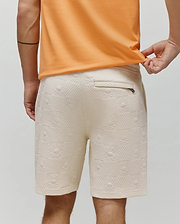 Mens Dustin Sweatshort in cream, featuring a relaxed fit and all-over textured jacquard checkerboard pattern with repeated Psycho Bunny skull logos and a zippered back pocket. (3)