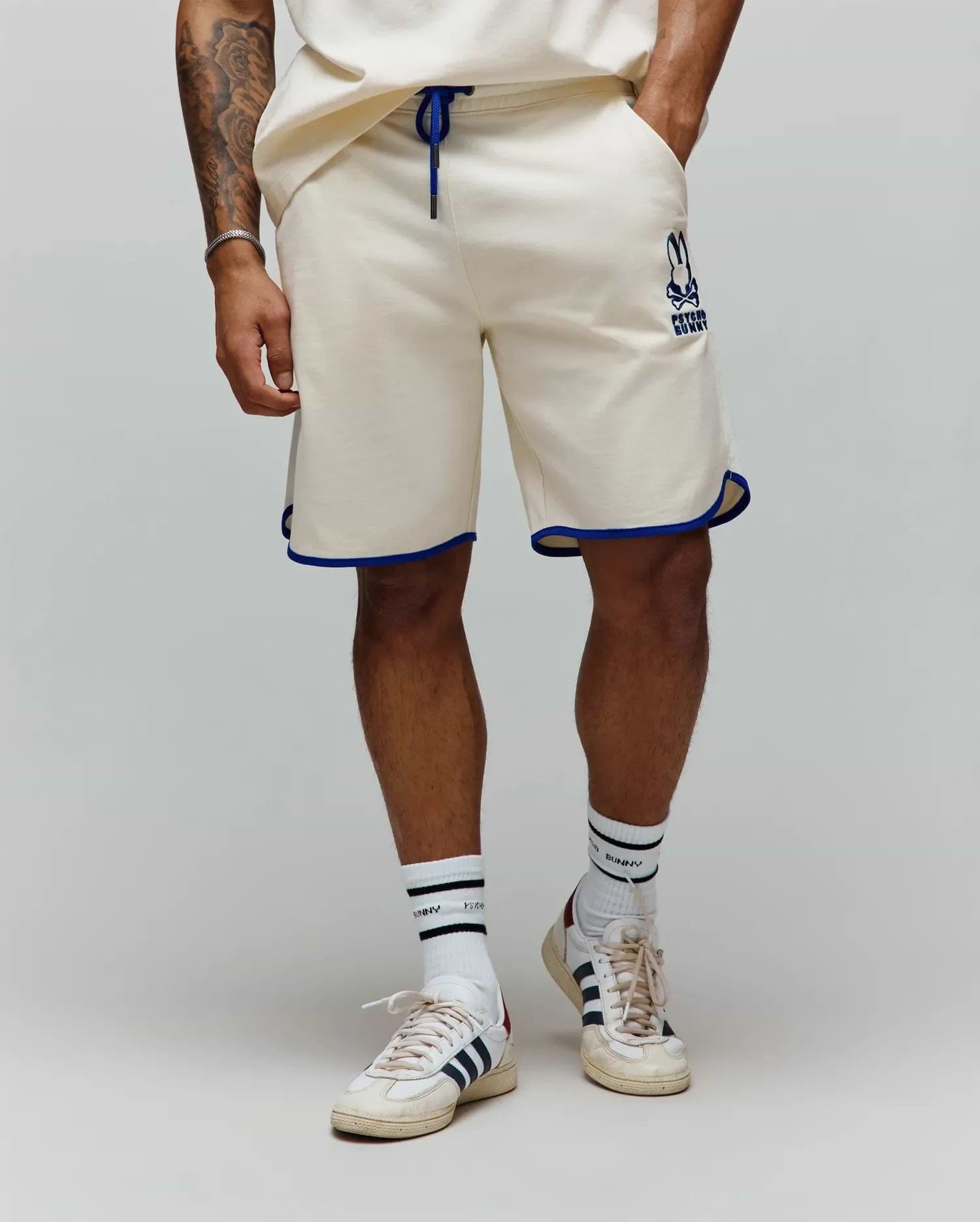 Mens Toby Short, cream french terry, relaxed fit shorts with royal blue drawstring and contrast piping. Features a medium-sized embroidered Psycho Bunny skull logo on the left thigh. (1)
